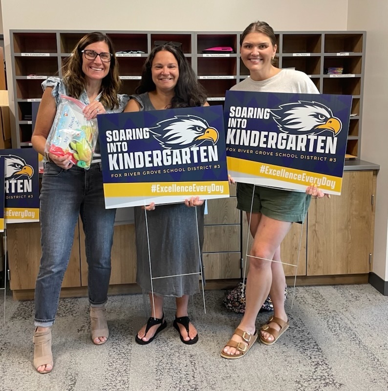 Mrs. Cole, Ms. Malone, and Mrs. Peters with the kindergarten signs & books