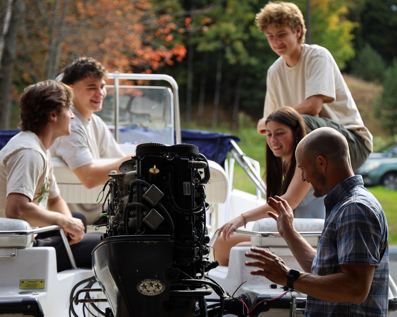 Marine Technology Instructor Josh Marlow works on a boat engine while students sitting in the boat observe.