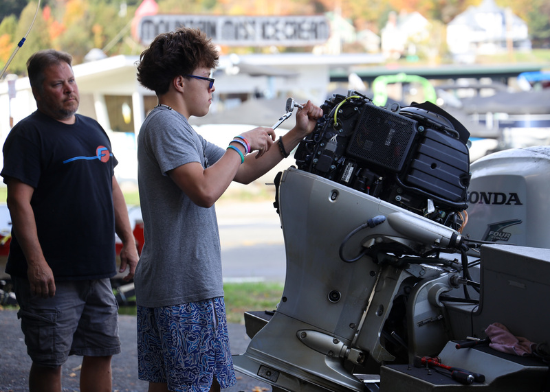 Maine Technology student works on a large boat engine at Fogarty's Lake Flower Marina in Saranac Lake while an employee supervises.