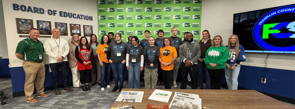 laser Program participants and leaders stand infront of FC SMedia Wall in board room.
