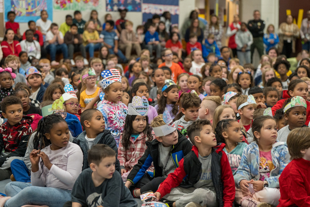 EES students sit on gym floor for veterans day assembly