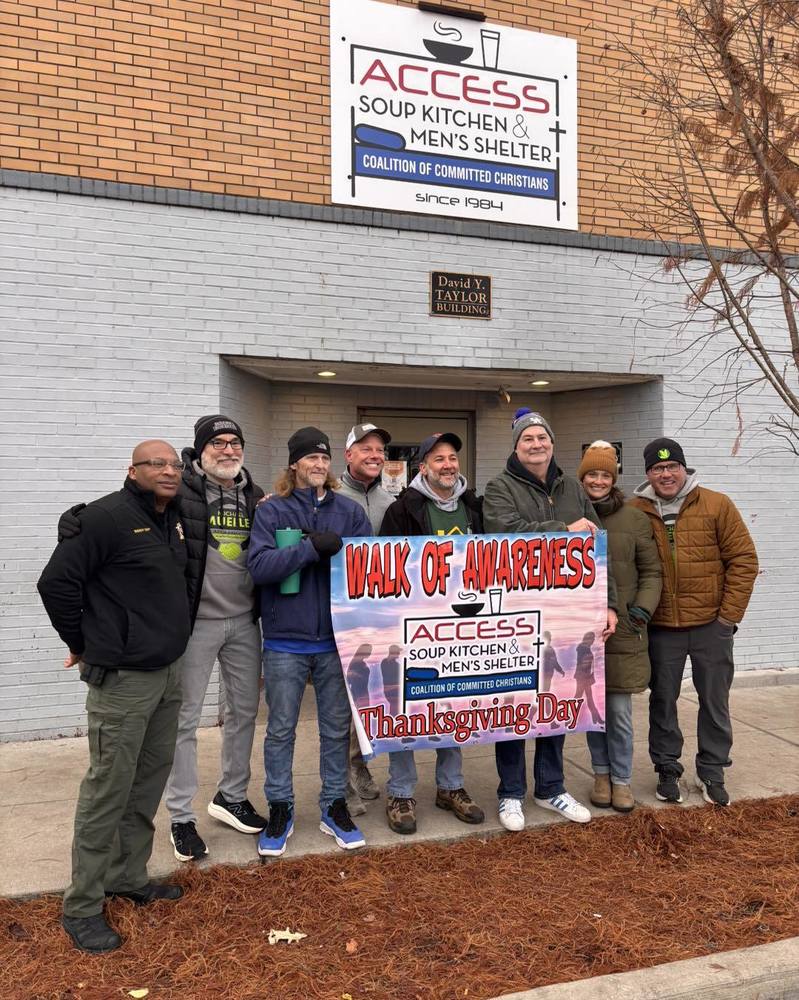 Leaders stand in front of the soup kitchen holding the walk of awareness sign.