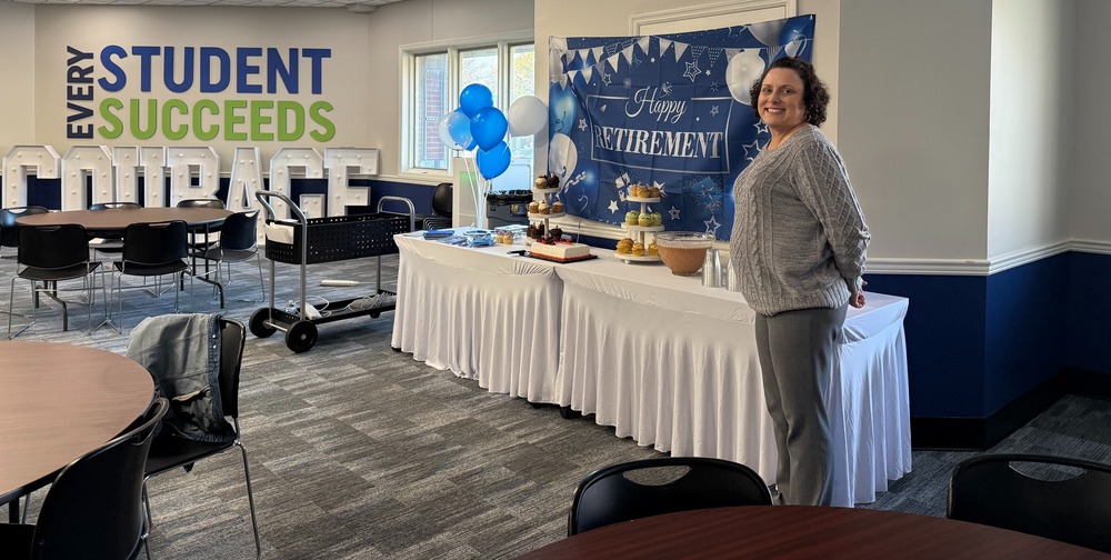 Julia stand in board room in front of a table with retirement treats.