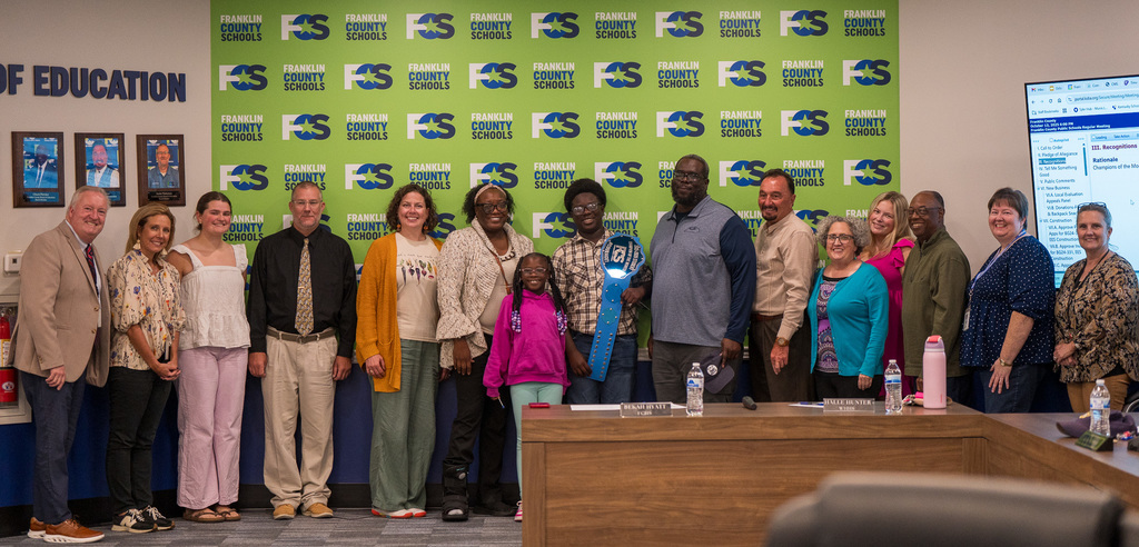 JJ Leach, Elkhorn Middle School, October Champion of the Month can be seen with his family and FCS Board members- in front of our legendary FCS Franklin County Schools green backdrop.