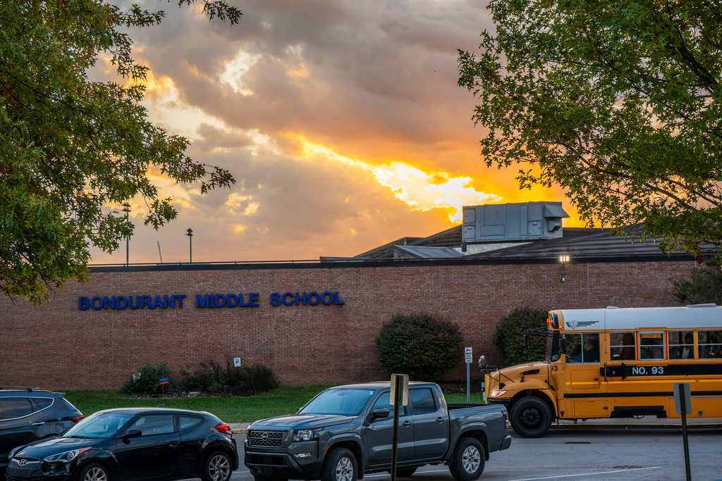 School bus in front of Bondurant Middle School. Morning sky in back ground and cars parked out front.