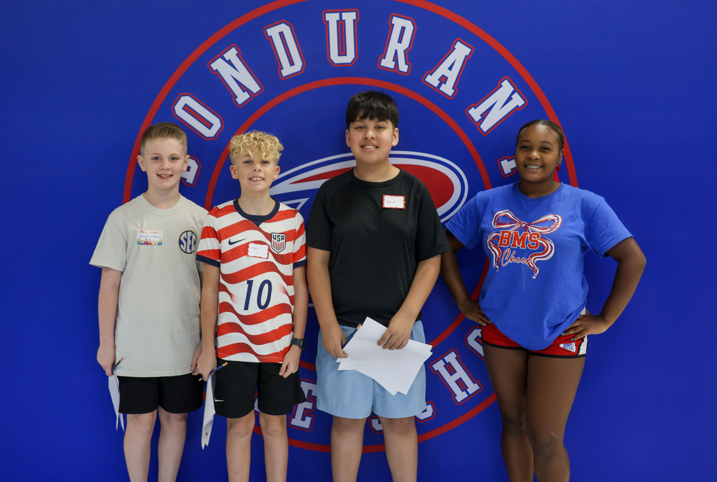 Group of four students stand in front of the Bondurant Middle School banner.