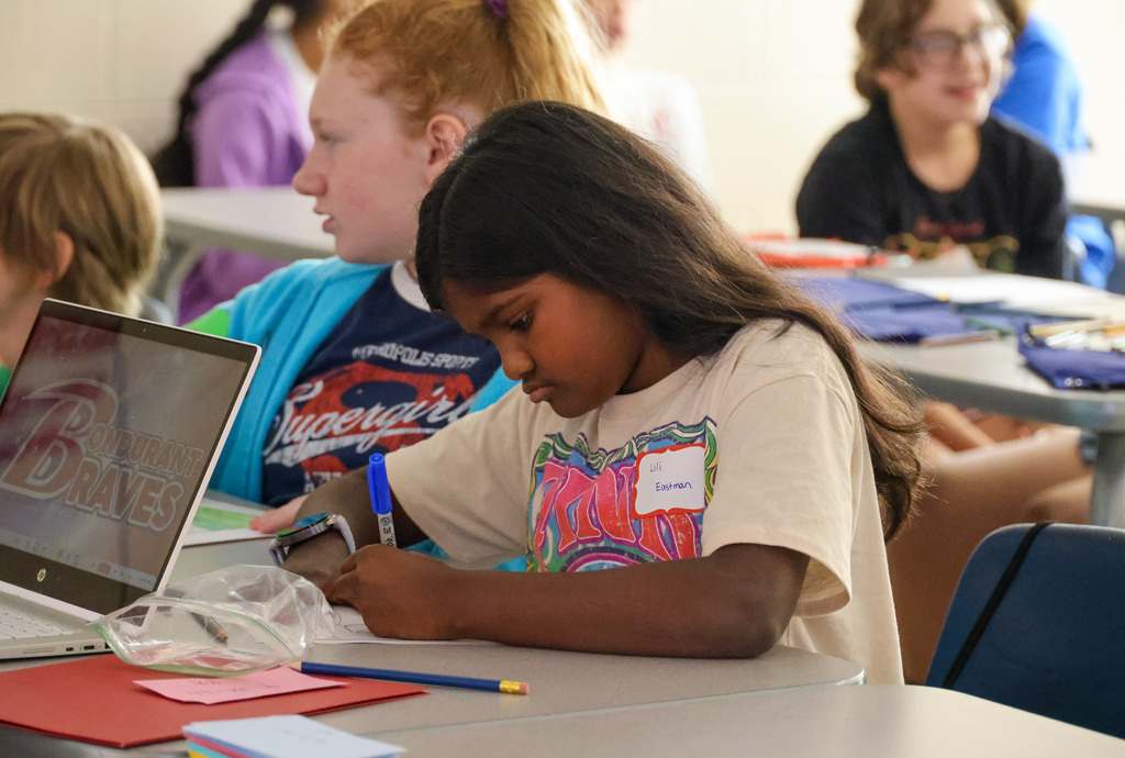 6th grade student writes on a sheet of paper in her classroom.