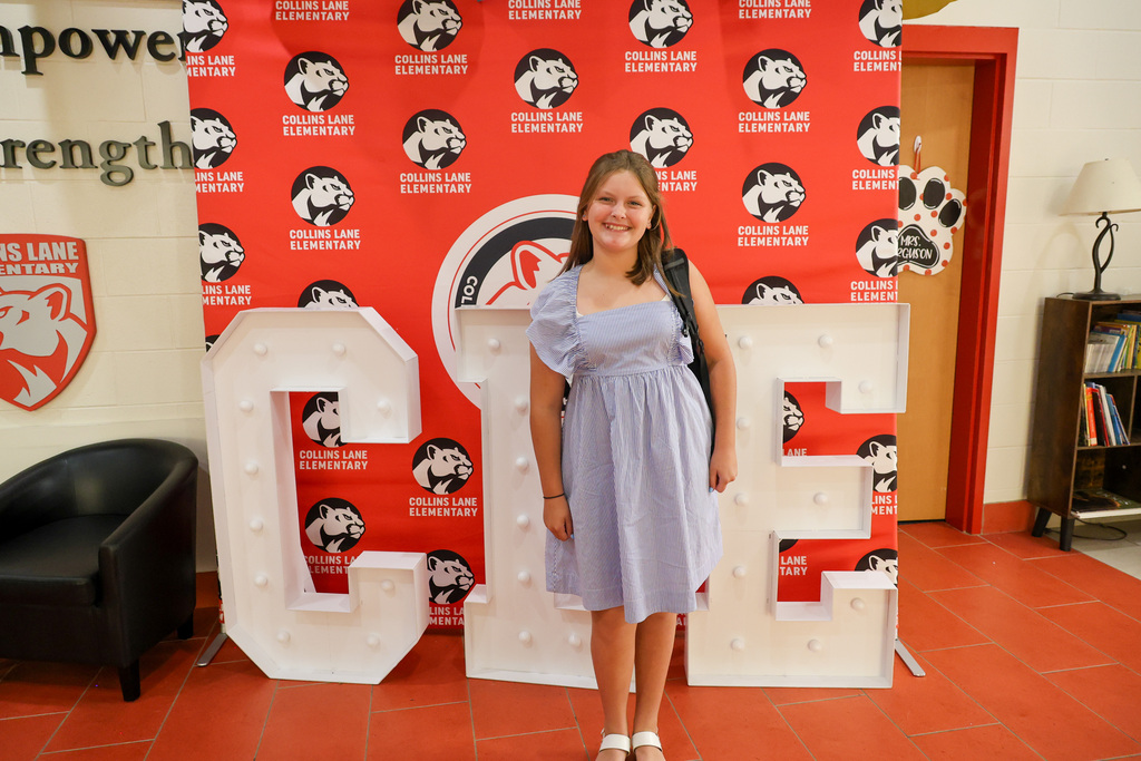 Collins Lane Elementary student poses in front of a "CLE" sign for the first day of school.
