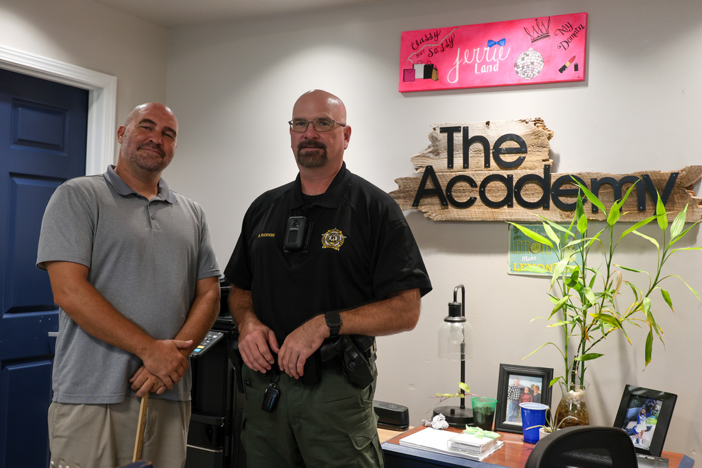 The Principal and School Resource Office smile next to a sign that says "Academy"
