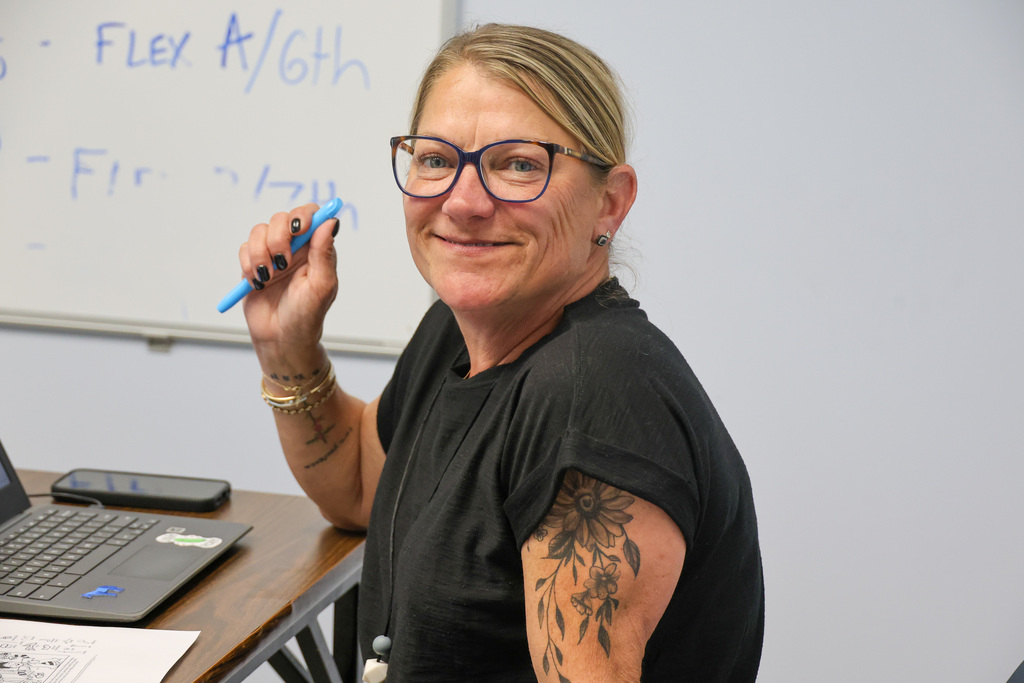 Teacher at the Academy smiles for a photo at her desk with a computer.