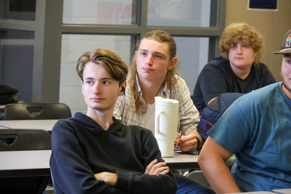 Students at desk listen to teacher.