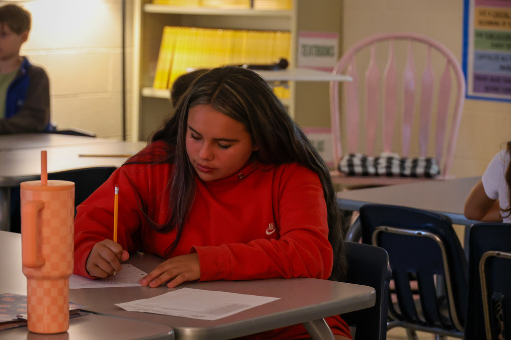 Student sits at desk writing with a pencil.