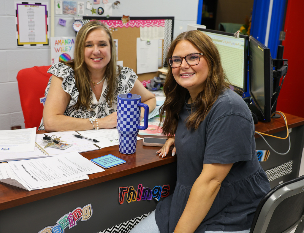 Two staff members sit at the desk and smile.