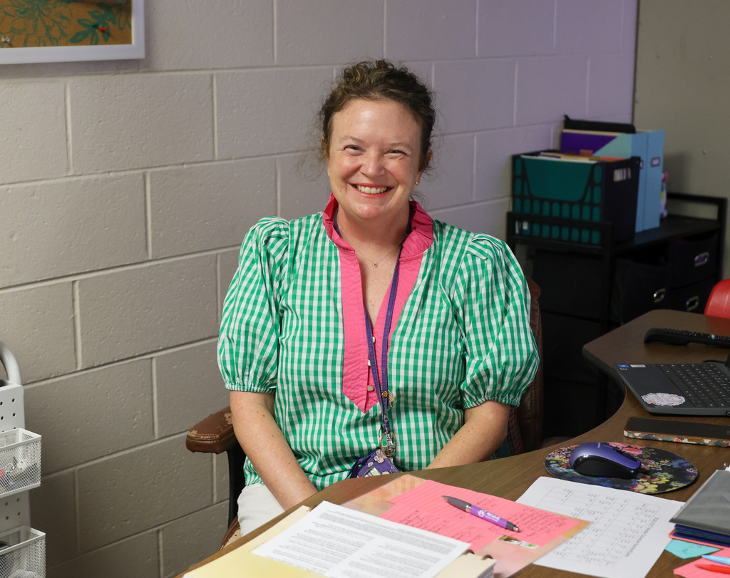 Staff member sits at desk and smiles.