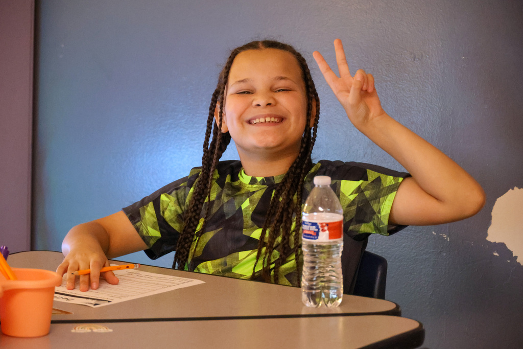 Student gives the peace sign and smiles while sitting at their desk.