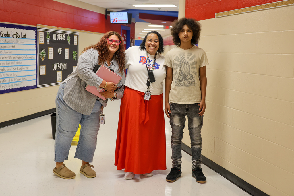 Two teachers and a student stand in the hallway.