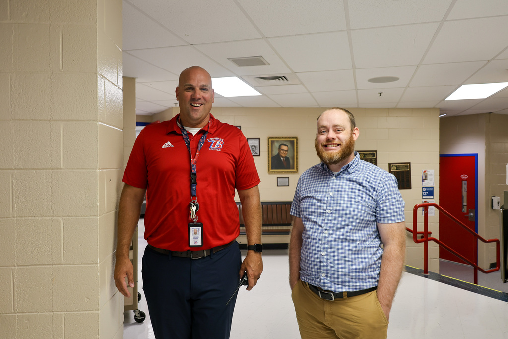 Two male teachers stand in the hallway with a smile for the first day of school.