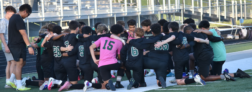 WHHS team huddles in a group on their knees.