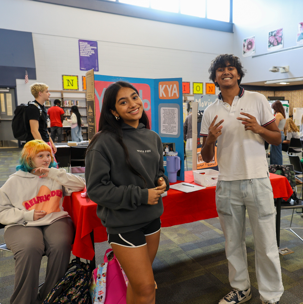 Students smile at the camera in front of their posterboard for the Y-club.