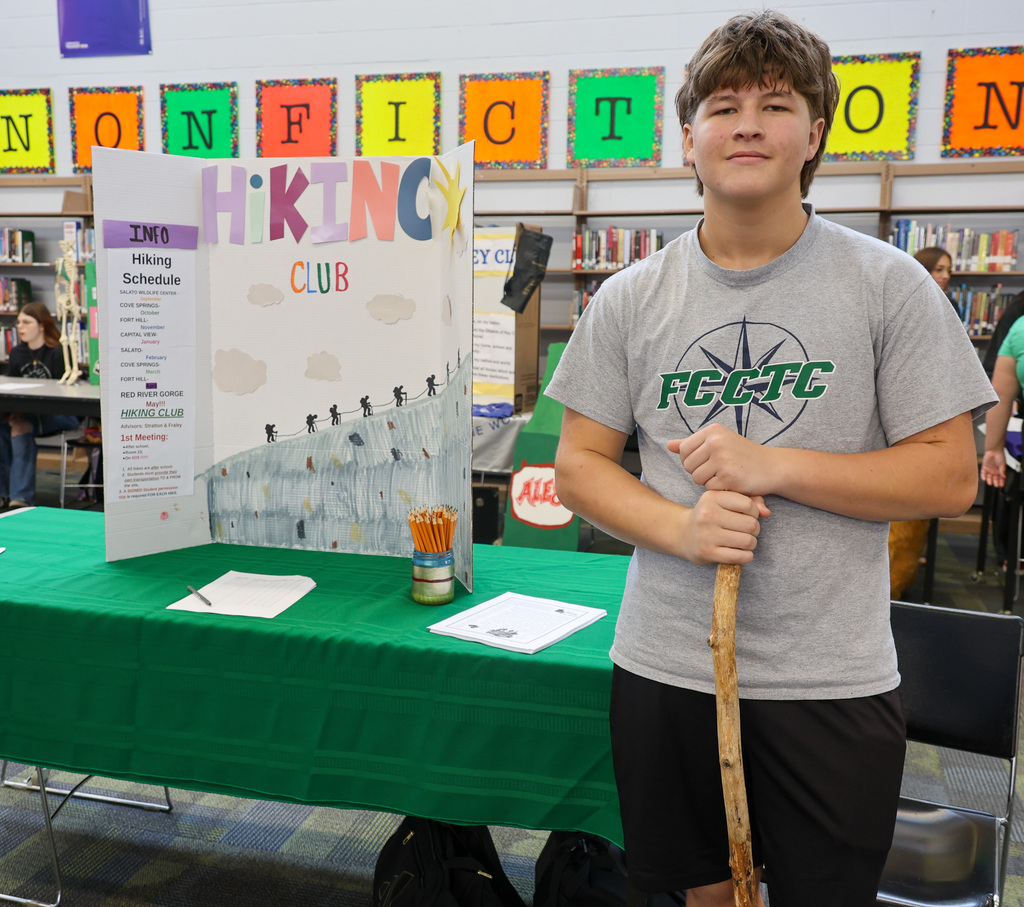 Student stands with his posterboard for the hiking club.