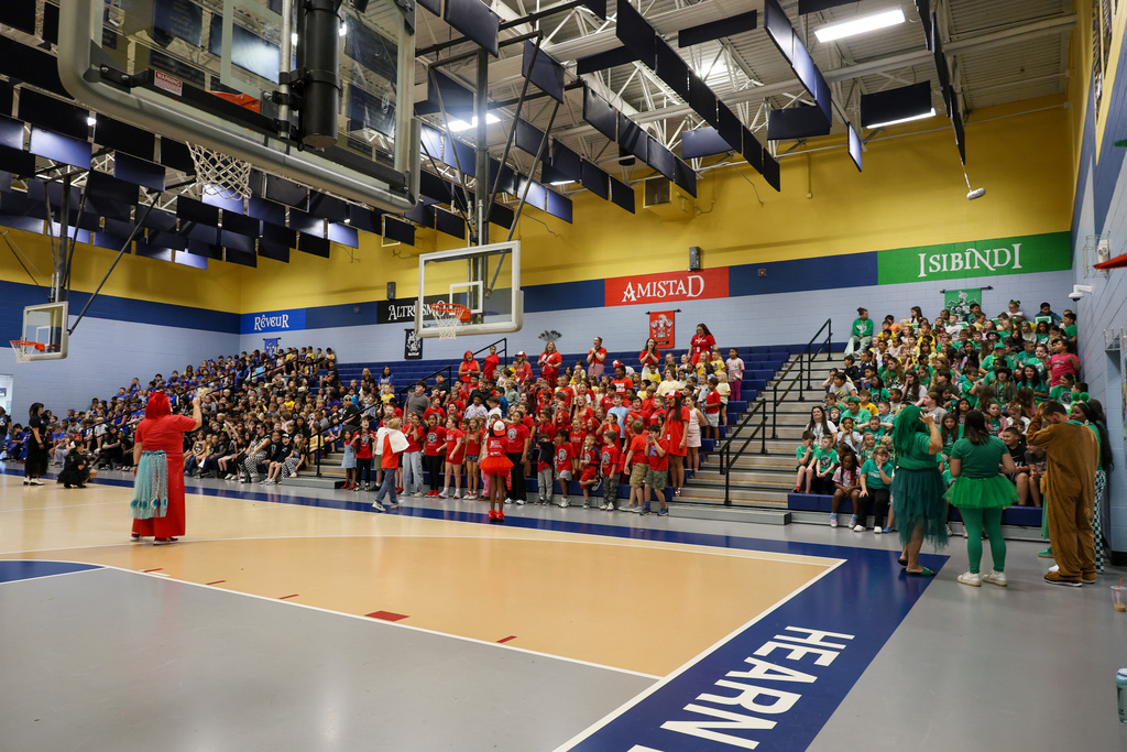 Wide shot of the whole gym. Students are sitting in their nests in coordinating colors (green, red, black, and blue).