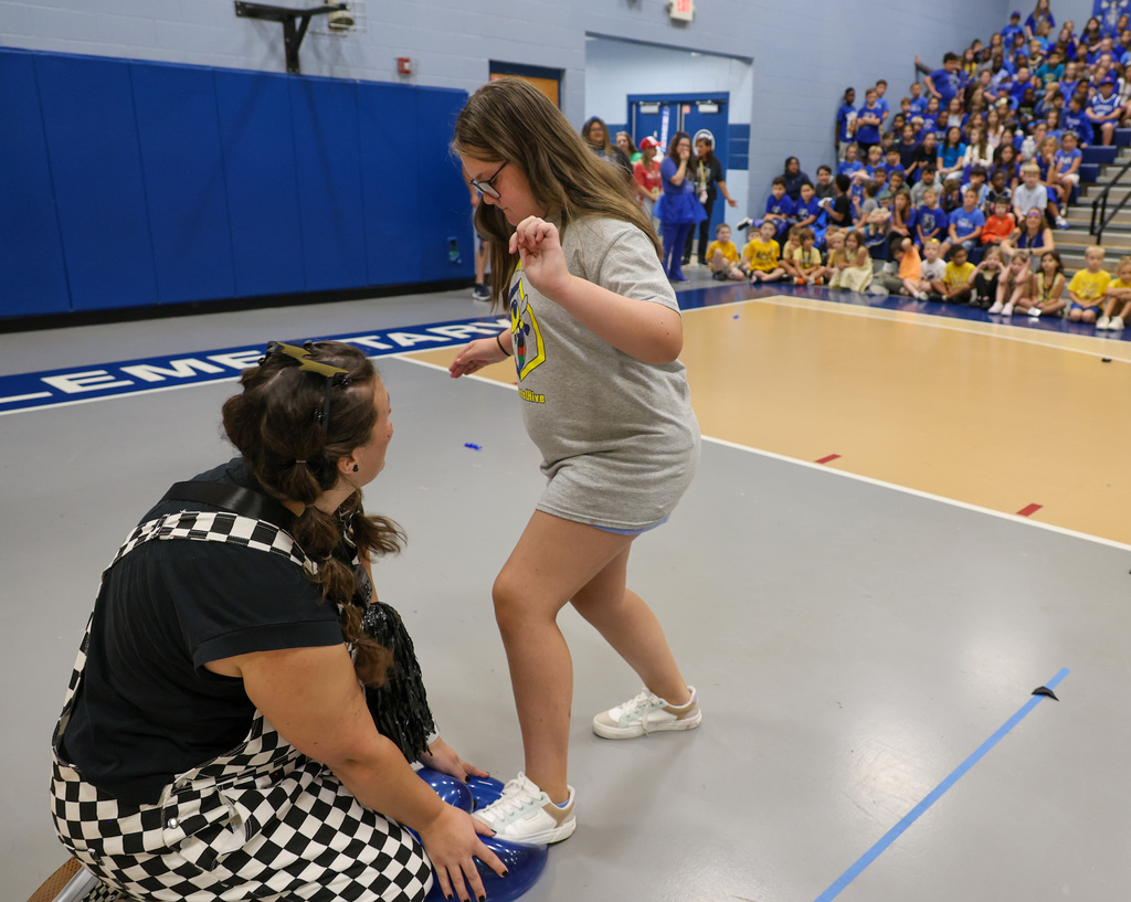 Staff member holds the ballon as a student steps on it to pop it.