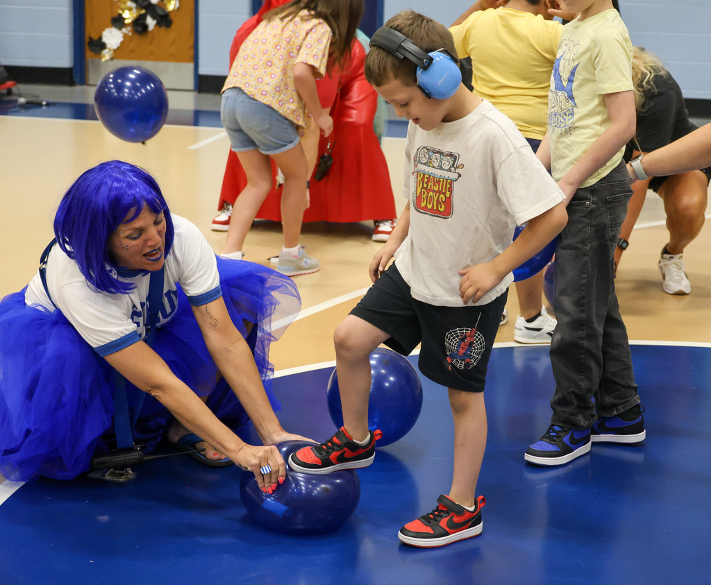 Principal Barton holds a blue balloon as a student steps on it to pop the balloon.