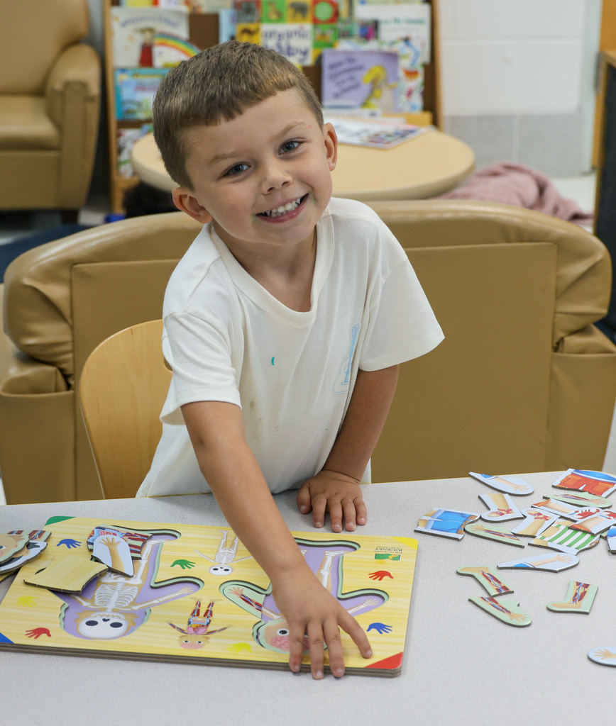 Preschool student smiles while putting together a puzzle.