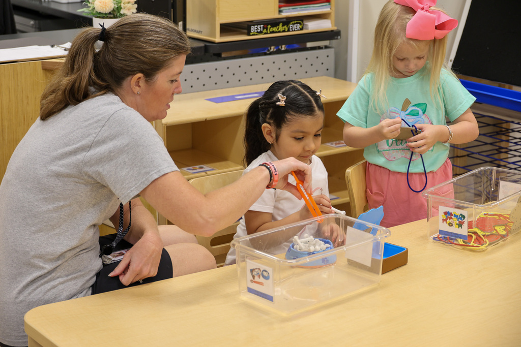 Teacher assists student as she plays with toys.