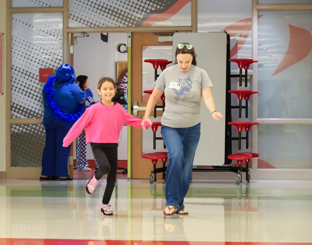 Student runs through the hallway with a parent volunteer to enter the gym where she will learn which house she is in.