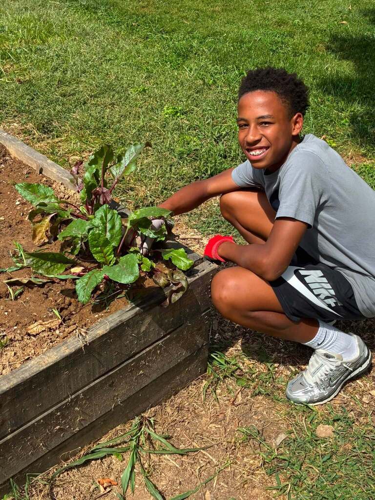 EMS student smiles next to a plant in the garden.