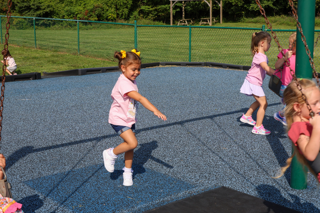 Preschool students pushes a student on the swing.