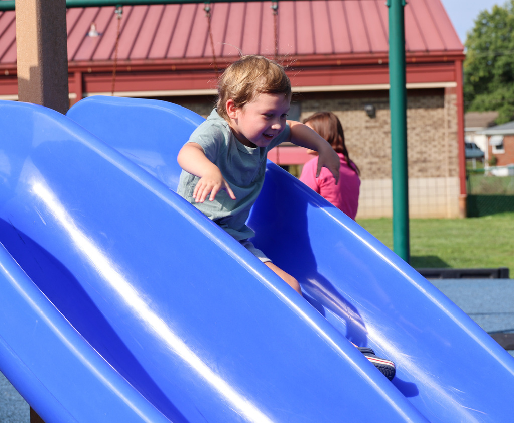 Preschool students goes down the slide.