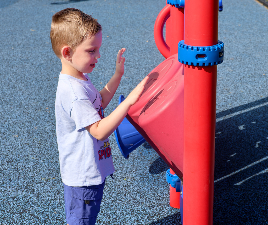 Preschool student plays the drums on the playground.