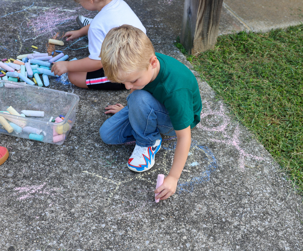 Preschool students uses chalk to color on the ground.