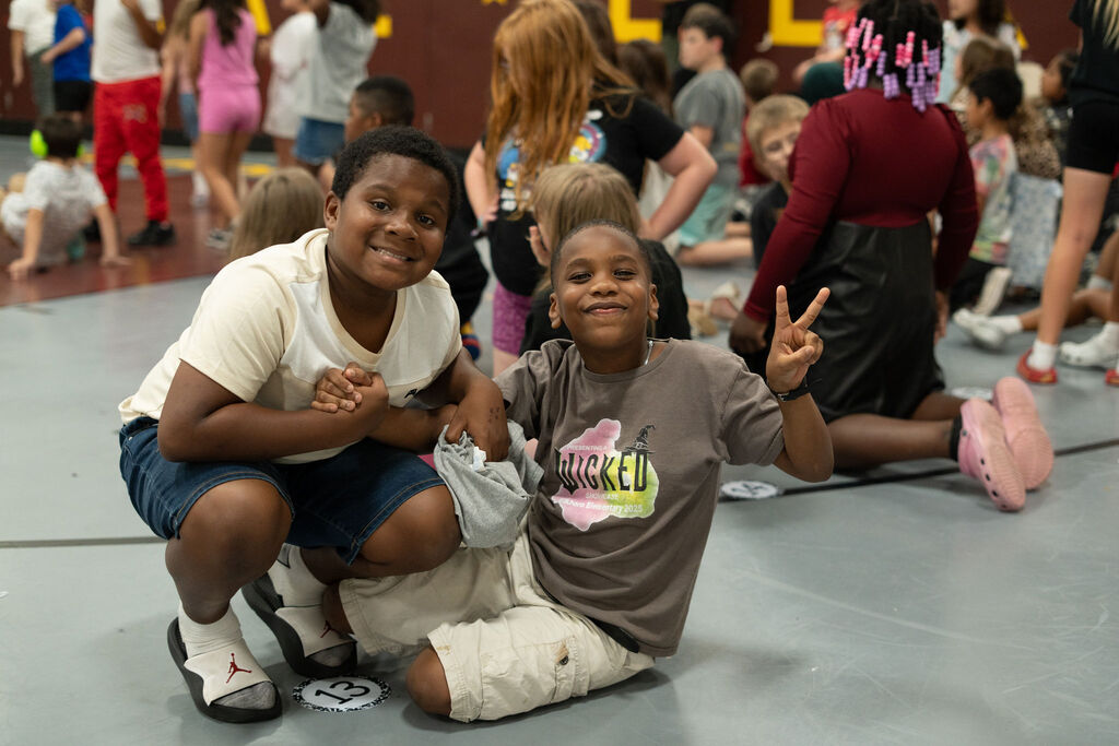 Two students smile and the kid on the right is giving the peace sign.