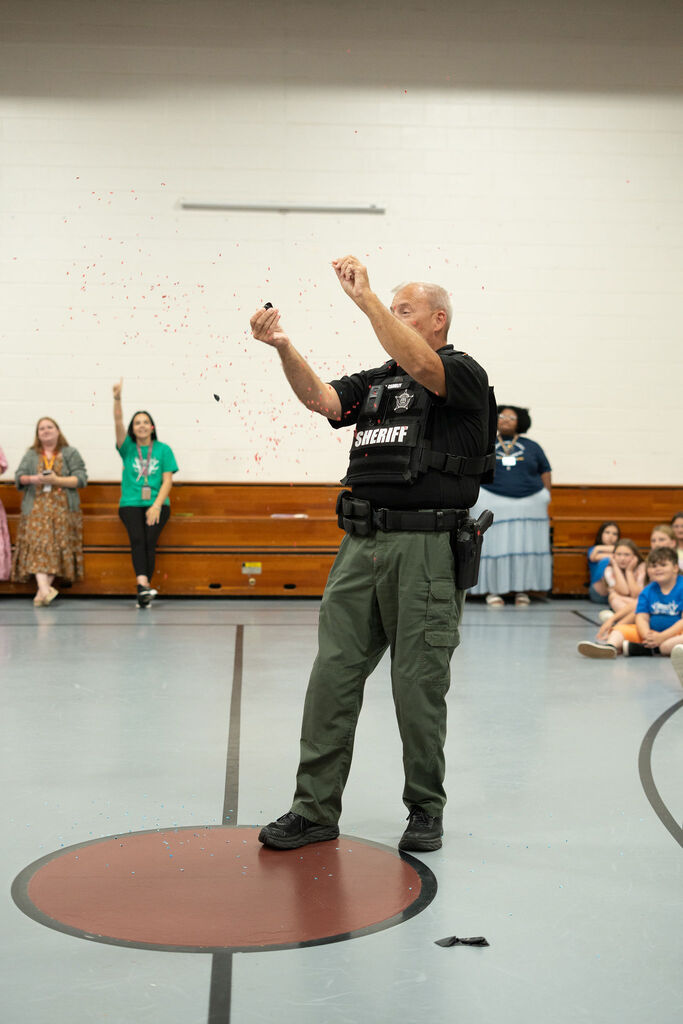 The school's SRO pops a balloon to reveal his herd. Red confetti is all around him.