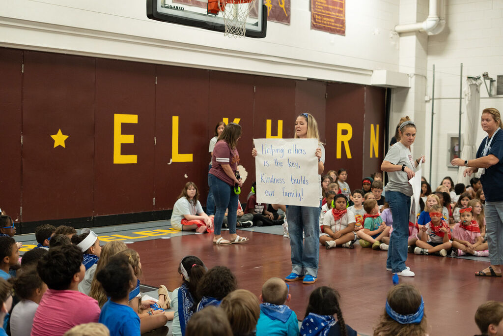 Teacher holding the "Kindness Herd" sign that reads "Helping others is the key. Kindness builds our family!"