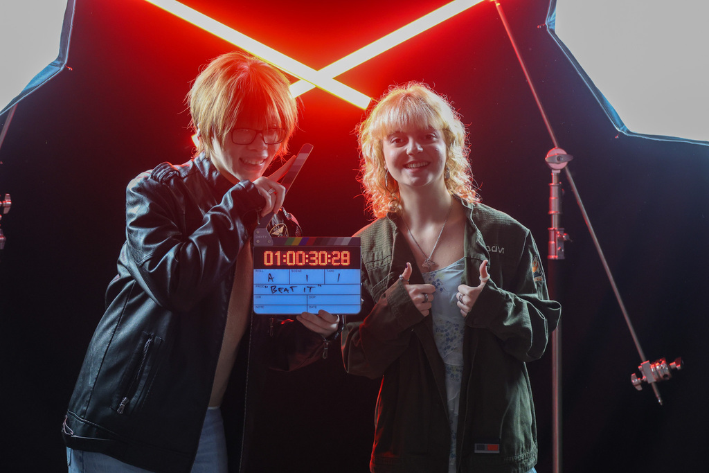 Students smile with red beam lights behind them and holding a movie marker and ready to say "Action"