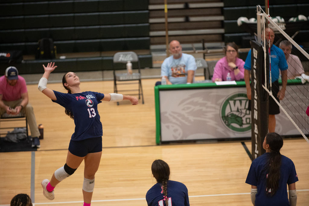 FCHS player jumps to spike the ball. Three other players on the court watch in ready positions.
