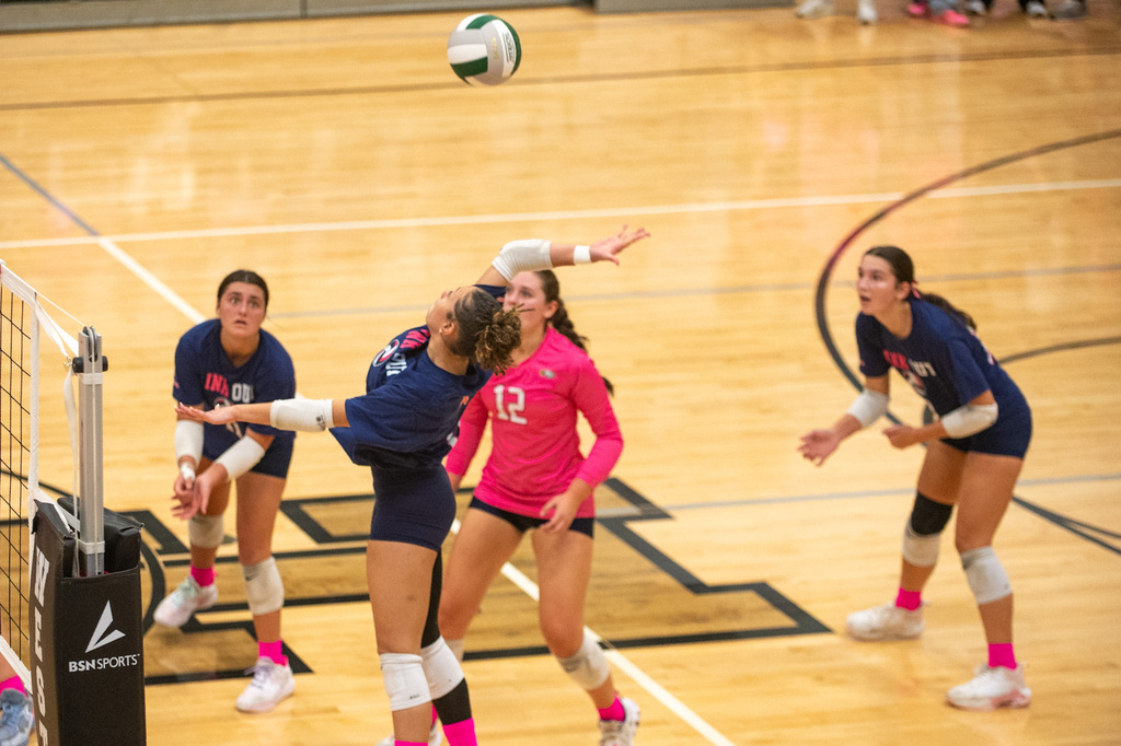 FCHS player jumps high to spike the ball over the net. Three other players stand in ready positions to assist.