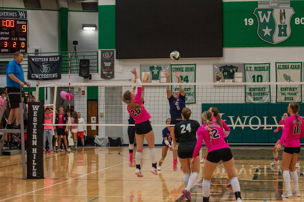 WHHS player jumps to hit the ball over the net and two FCHS players jump to block the ball at the net.