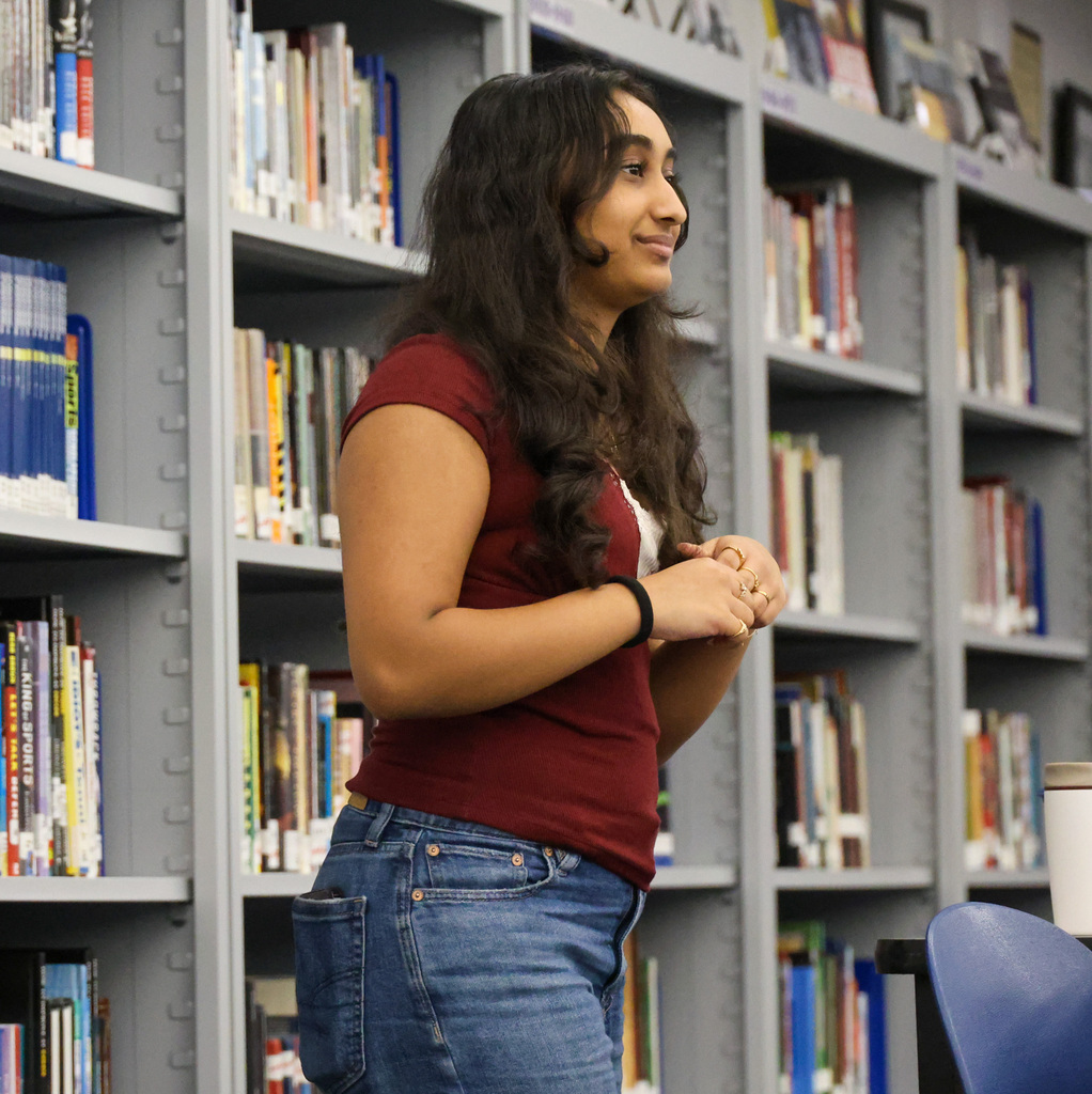 Student Voices Committee member. The student is standing at the front of the library as she speaks to the group.