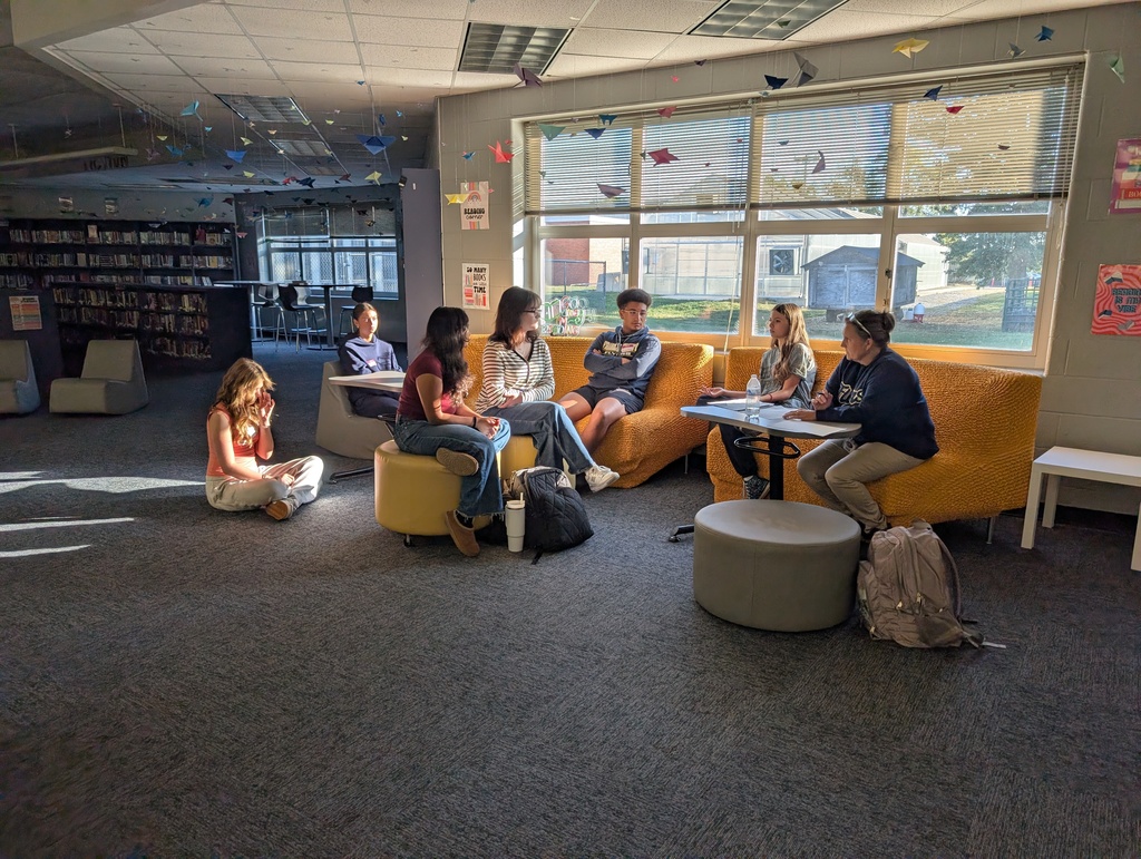 Students sit on couches and stools with Assistant Superintendent Tammy McDonald to work on a project.