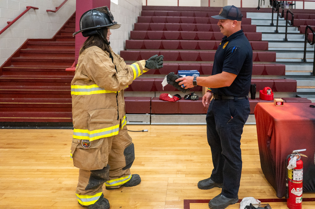 Student wears firefighter uniform and talks with a firefighter.