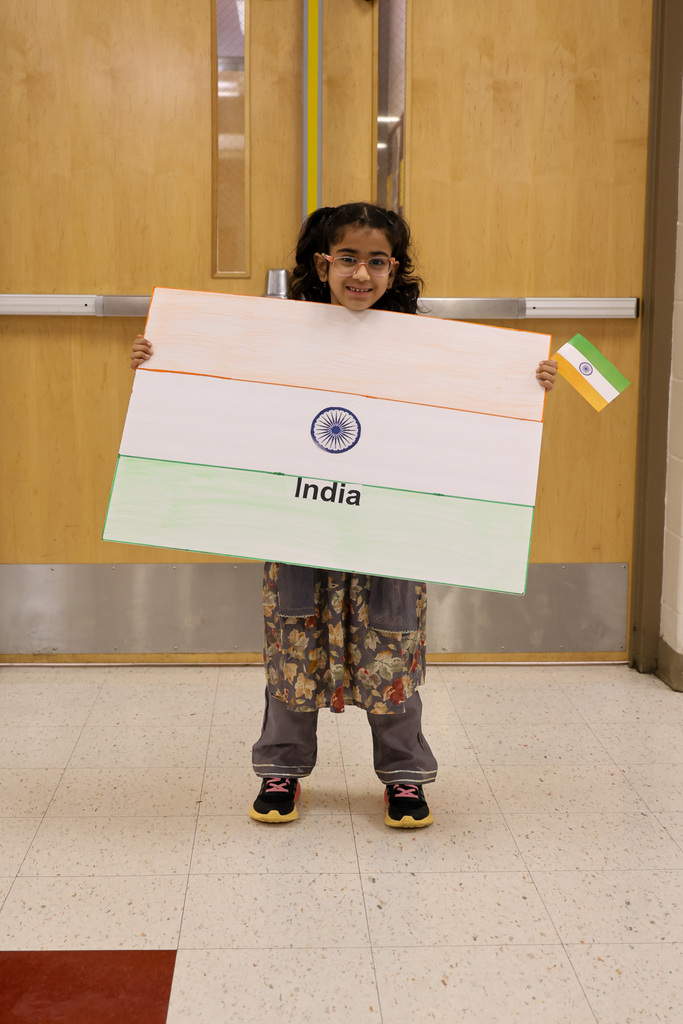 Students holds sign with the flag of India. She is also holding an India flag and smiling.
