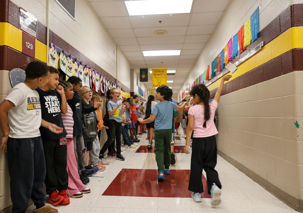 Students wave their flags as they walk through the hallways. Students in the hallway are cheering them on.