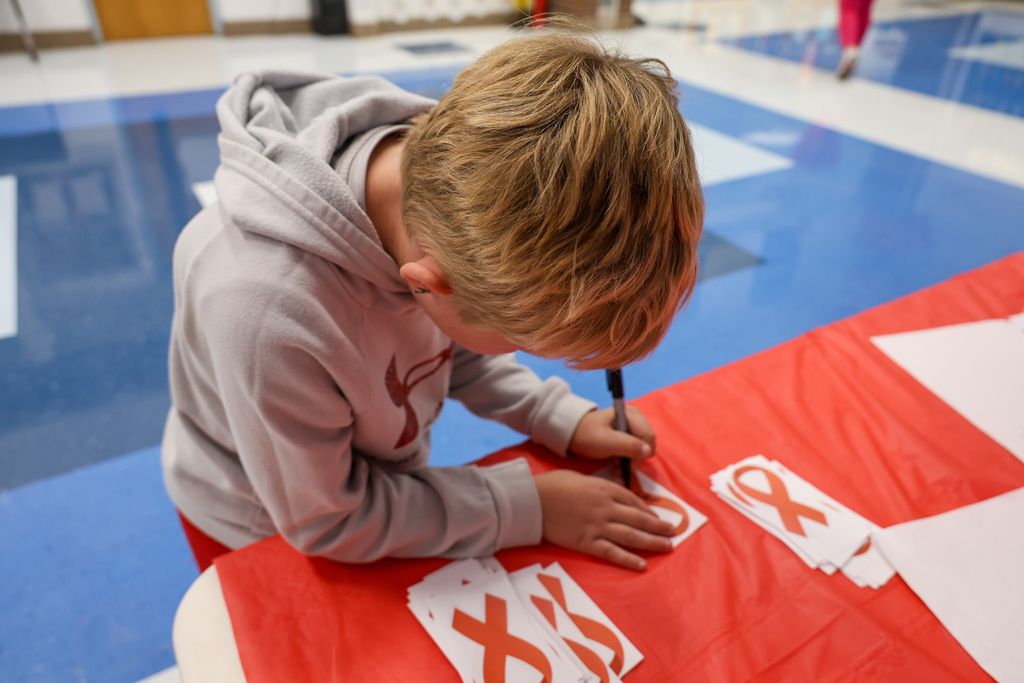 Student writes his name on a red ribbon.