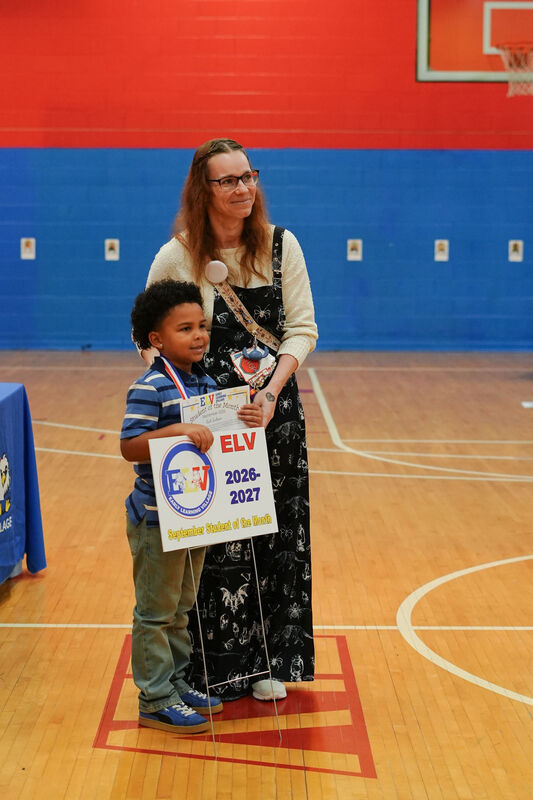 ELV student stand with his teach holding a yard sign that states he is the student of the month.