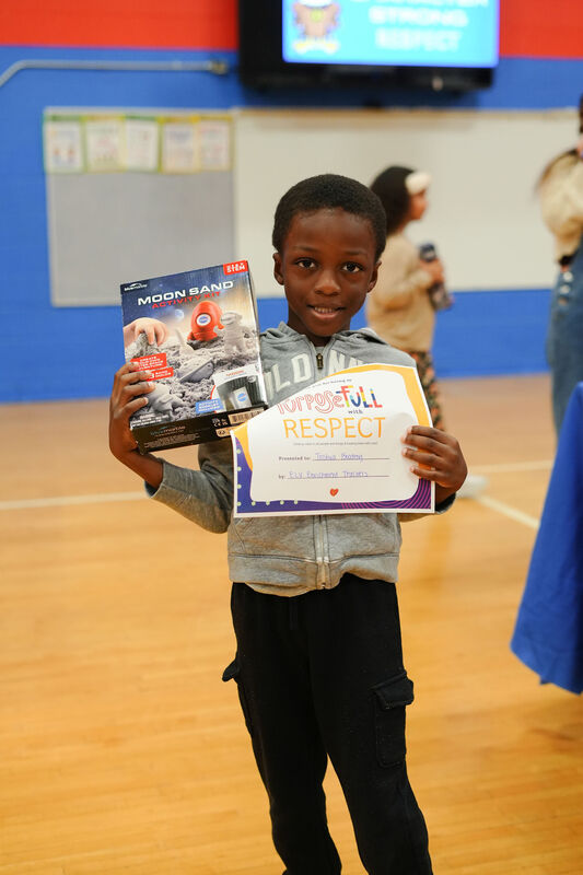 ELV students poses holding his "Purposeful with Respect" certificate and Moon Sand Activity Kit.